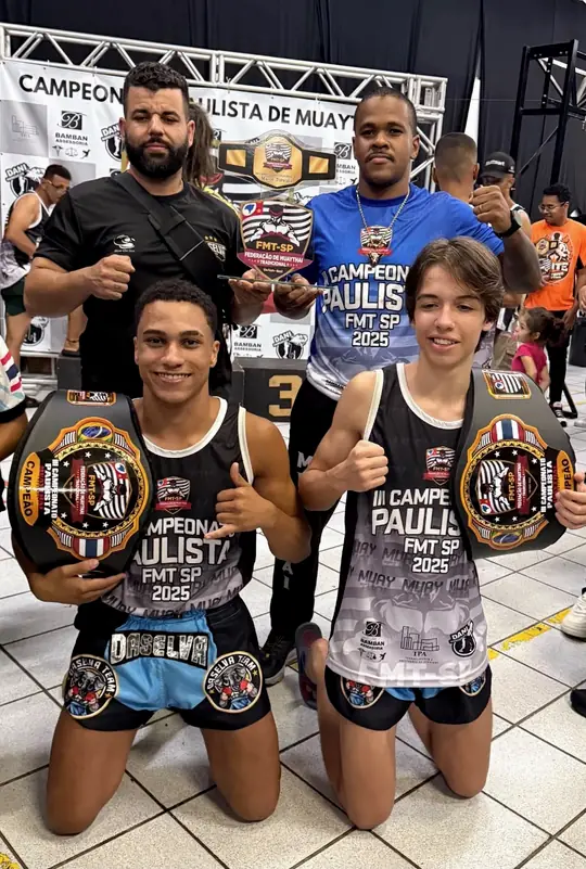 Professor Rubens com atletas da DaSelva Team segurando os cinturões do Campeonato Paulista FMT-SP 2025