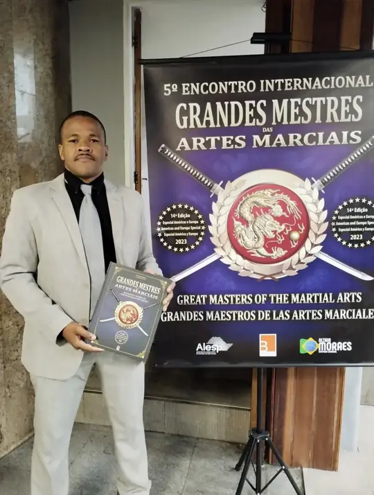 Professor Rubens de terno segurando o livro Grandes Mestres das Artes Marciais no 5º Encontro Internacional